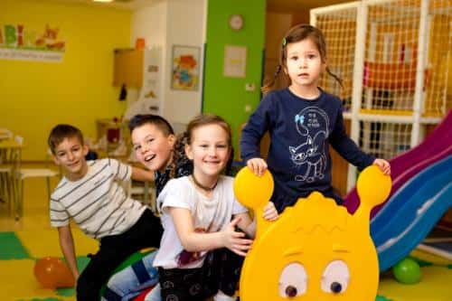 Skupina otrok se smeji med igro na rumenem igralu v igralnici